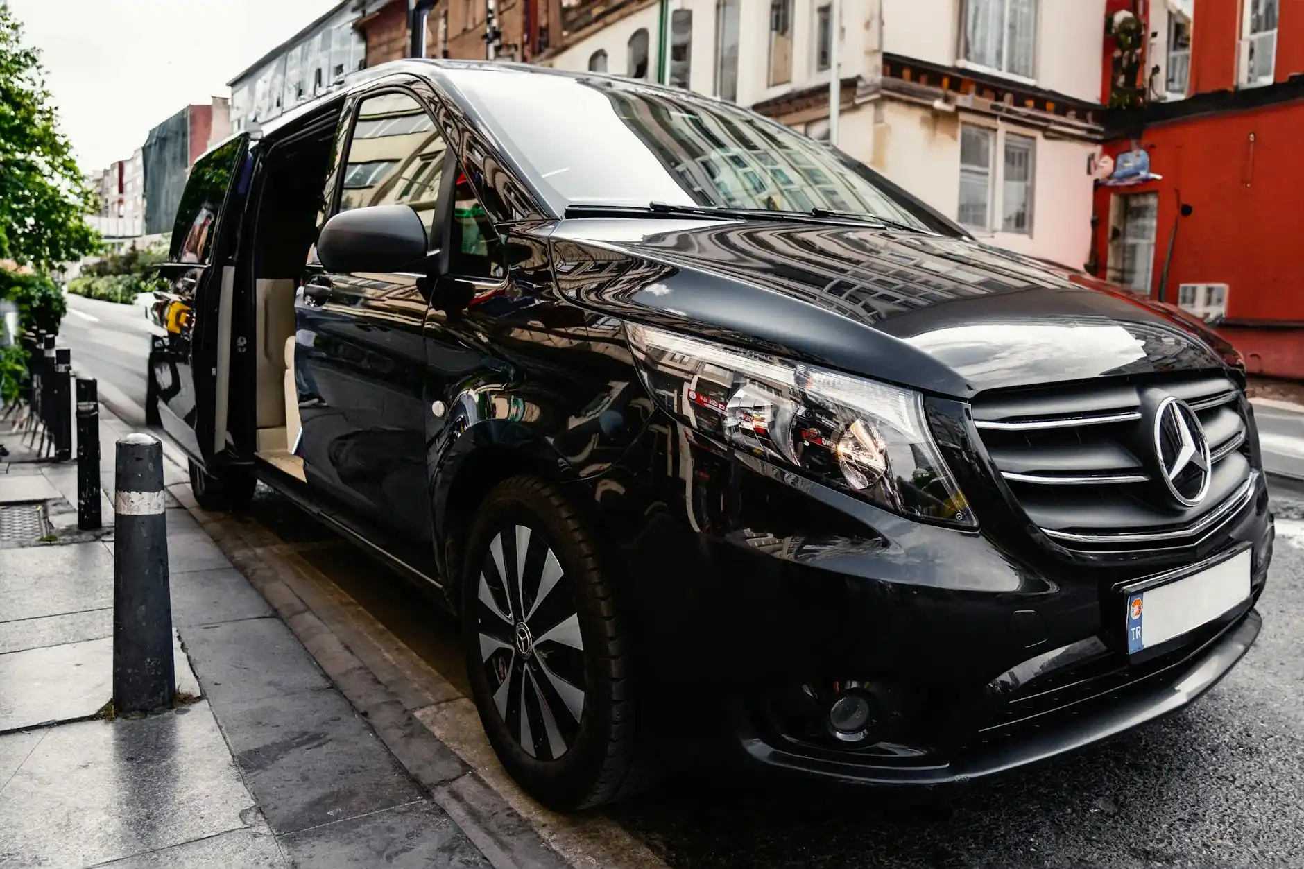 luxury black SUV chauffeur vehicle parked curbside outside a downtown Seattle hotel with Bell Street and skyline visible, chauffeur assisting guest with garment bag