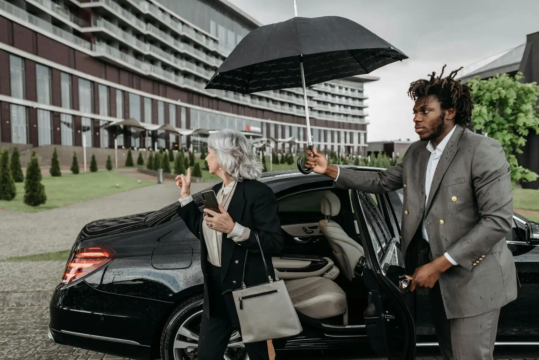 black luxury executive sedan pulling up to a glass office tower in downtown Seattle on a rainy morning, business travelers with briefcases entering the vehicle, skyline and wet ...