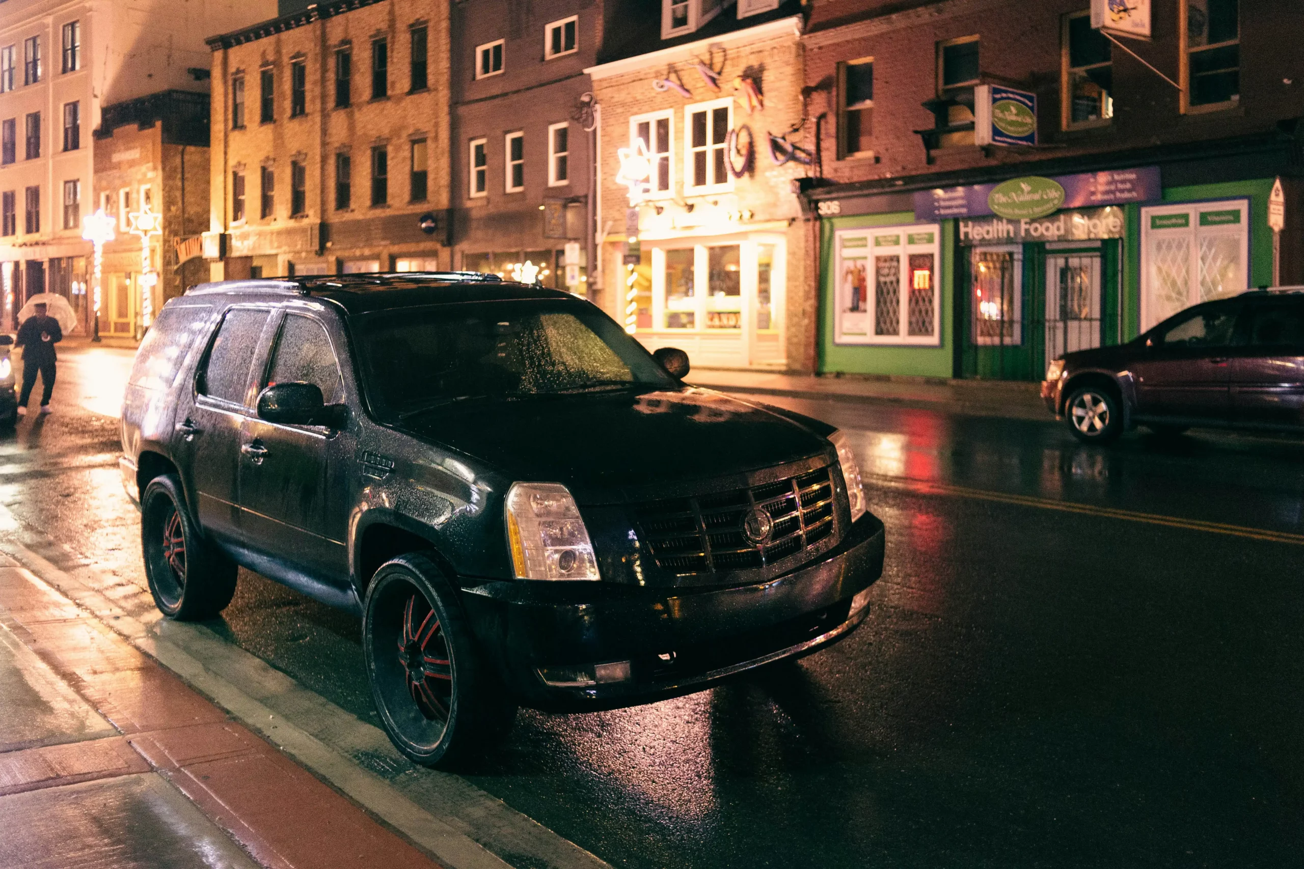 professional chauffeur checking a holiday transportation schedule beside a polished black SUV in front of a Seattle waterfront hotel, light rain and festive wreaths visible