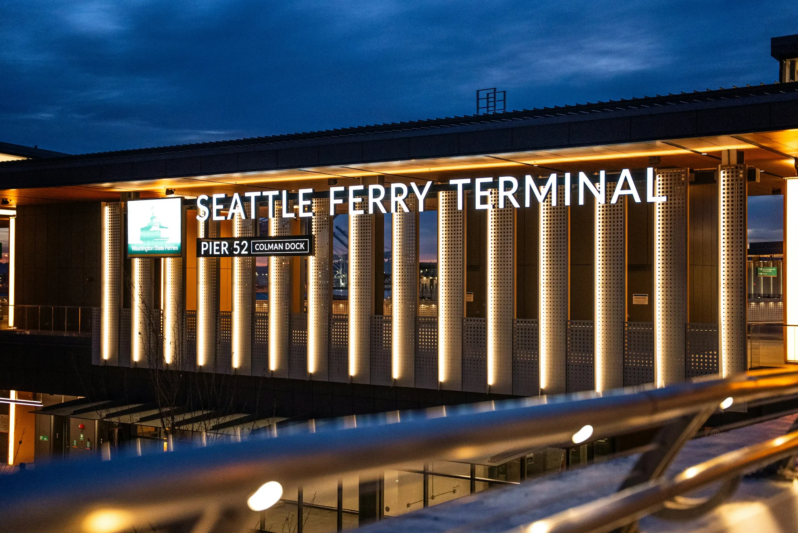 black luxury limousine parked at Seattle-Tacoma airport curbside at dusk, driver in dark suit holding tablet, city lights and light rain reflecting on pavement