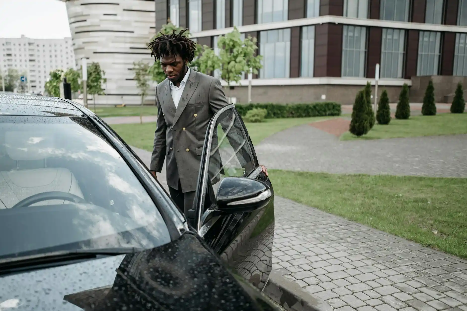 black executive sedan pulling up to Seattle-Tacoma International Airport arrivals curb at dusk, soft rain on pavement, illuminated terminal signage, professional chauffeur openi...