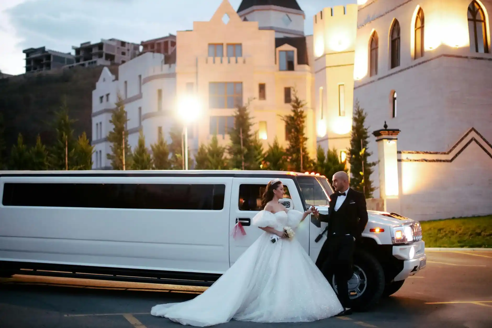 white stretch limousine parked in front of a Seattle waterfront wedding venue, bride and groom near the door, floral arrangements, evening lights reflecting on Elliott Bay