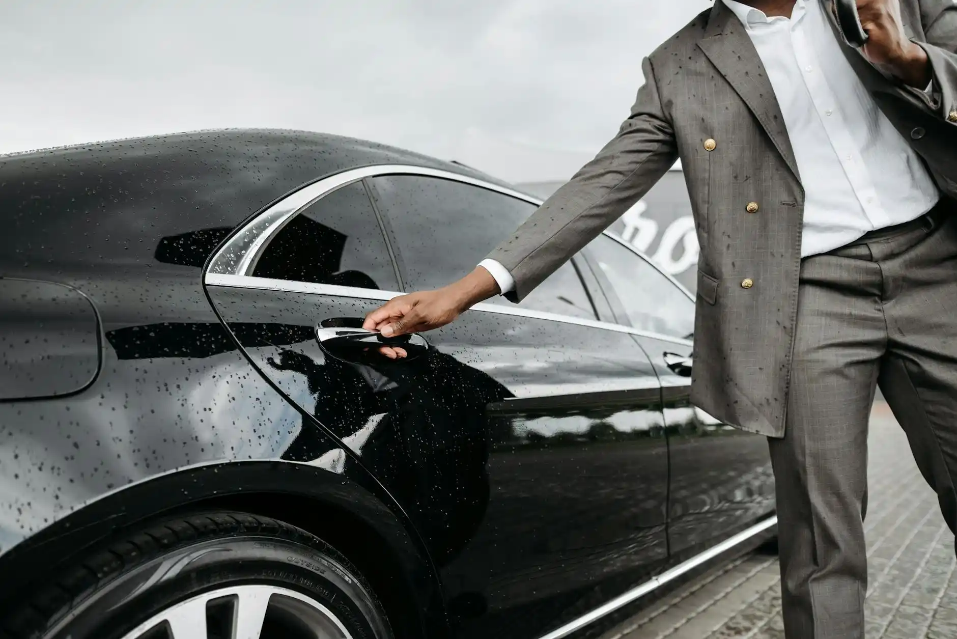 black luxury limousine parked at a covered hotel entrance in downtown Seattle at dusk, chauffeur in dark suit opening the rear door, city lights reflecting on wet pavement