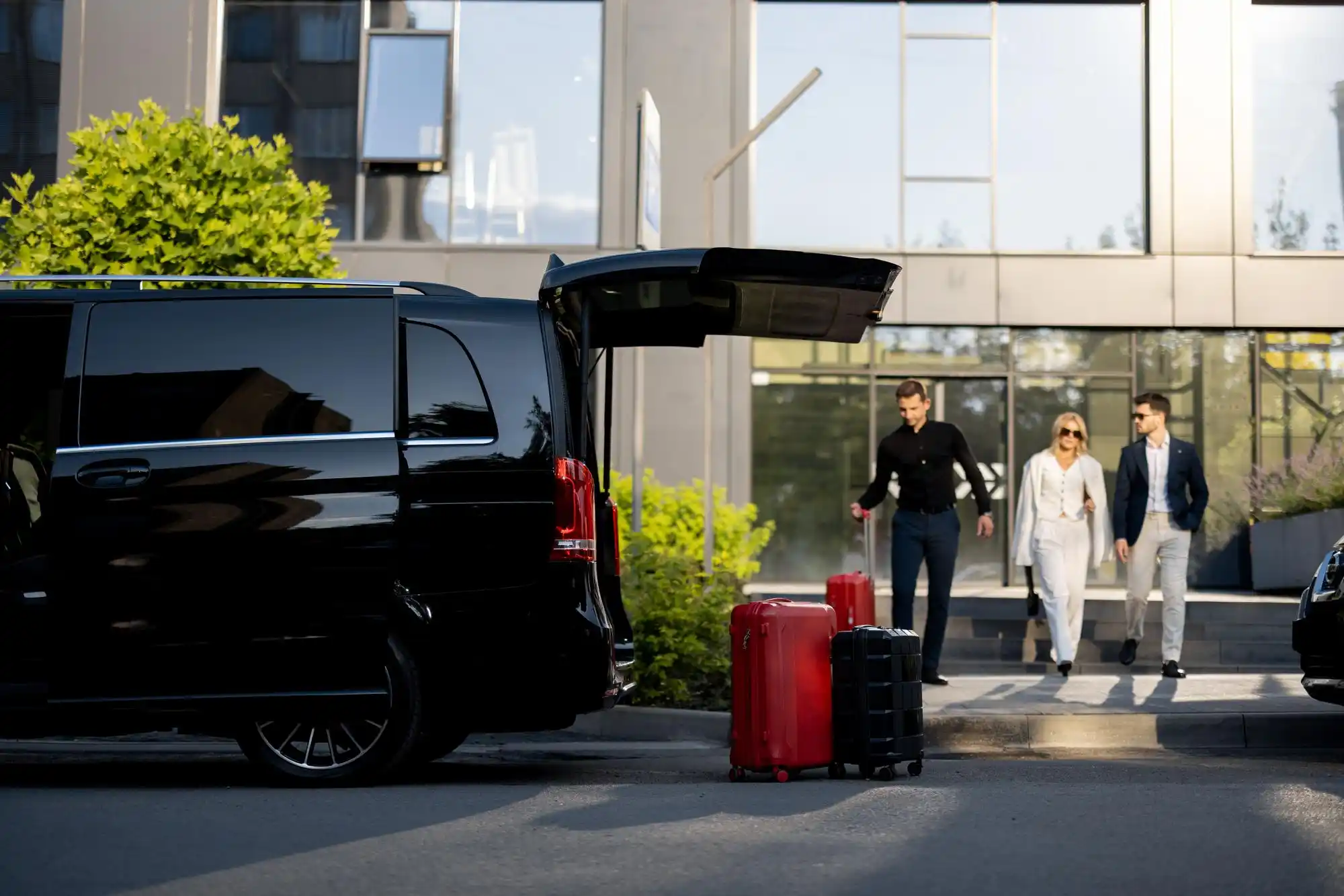 chauffeur loading several large suitcases into a luxury black SUV outside a Seattle waterfront hotel, early morning mist, cruise terminal and ferries visible in the distance
