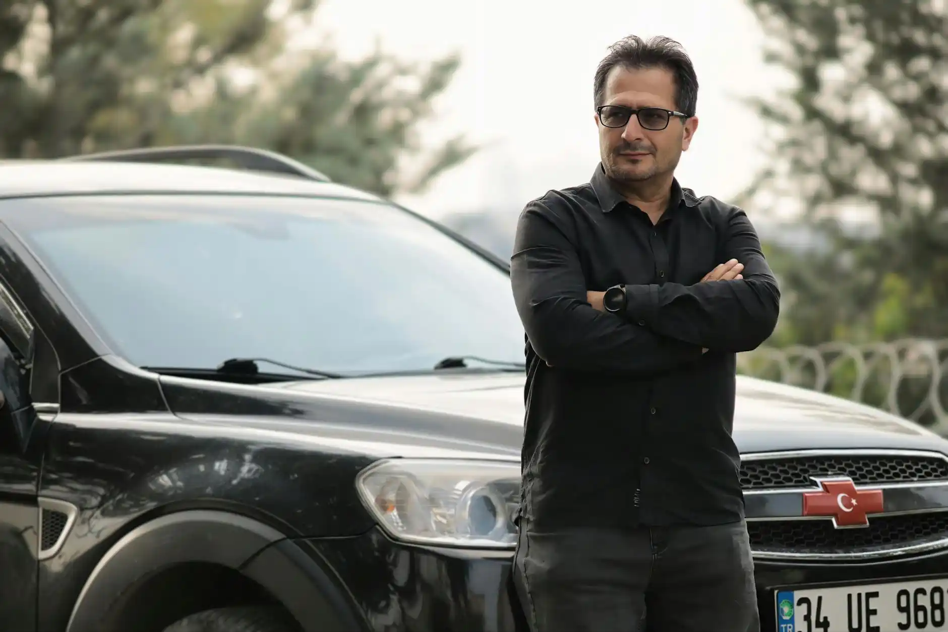 professional chauffeur in dark suit and tie standing beside a polished black luxury SUV at Sea-Tac airport arrivals, holding luggage trolley, clean modern terminal setting