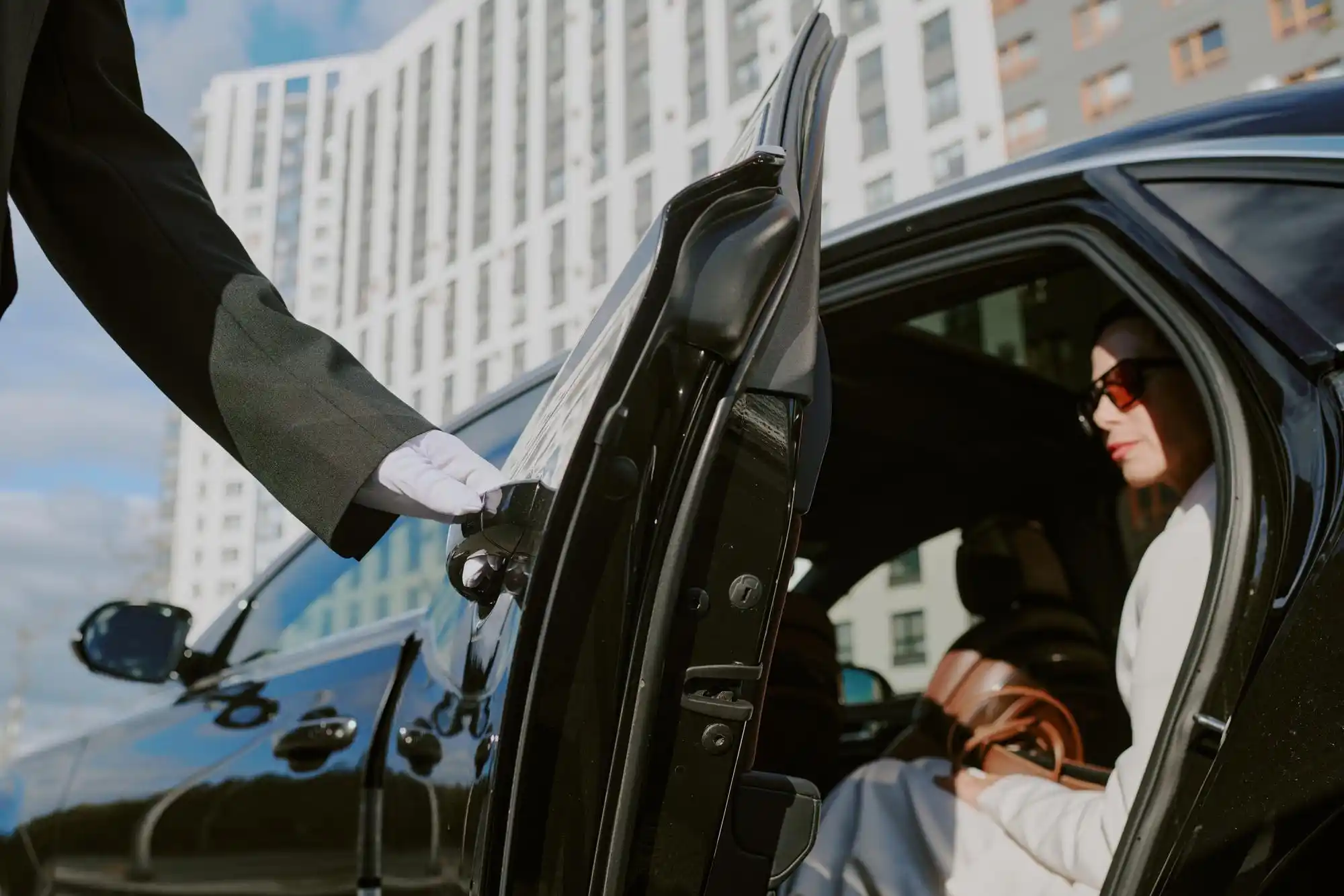 black luxury limousine pulling up curbside in downtown Seattle at sunrise with Space Needle in background, professional chauffeur opening rear door in crisp suit, wet pavement r...